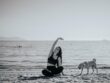 Grayscale Photo of Woman Doing Yoga on the Beach