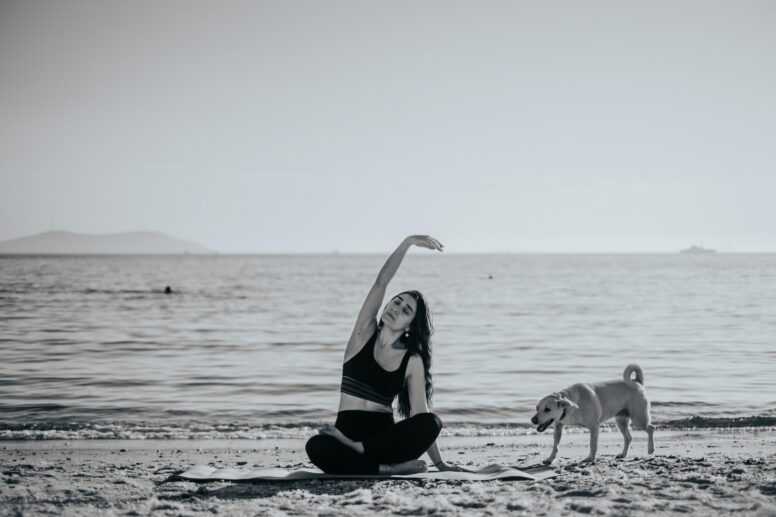 Grayscale Photo of Woman Doing Yoga on the Beach